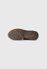 Brown rubber shoe sole with textured patterns, including grooves and circular indentations, designed for traction and grip.