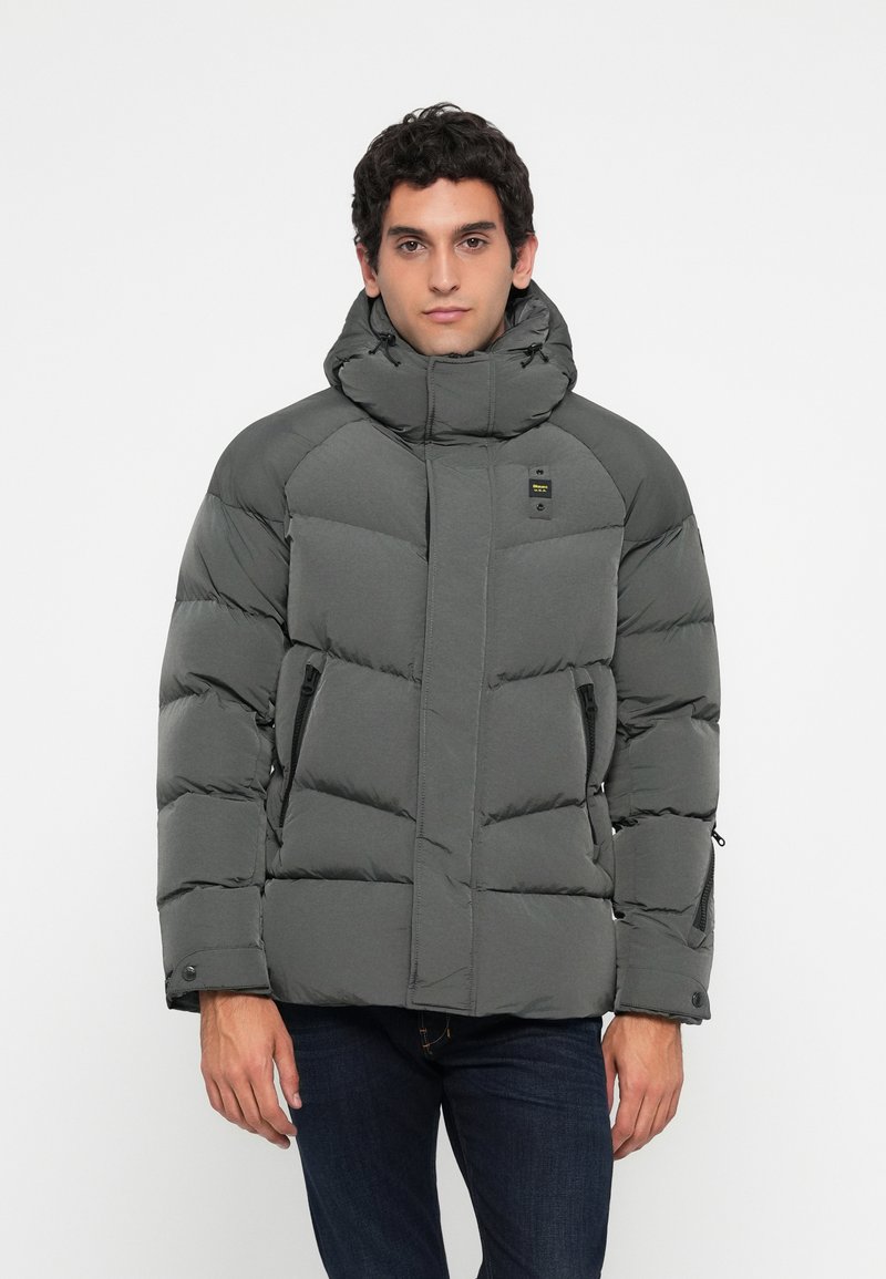 Chaqueta de invierno gris acolchada con cuello alto, bolsillos con cremallera y puños elásticos, que presenta una textura suave y un diseño elegante.