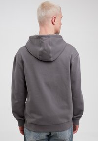 Grå sweatpullover med en stor hætte, ribbede manchetter og nederkant, lavet af blødt stof; vist fra ryggen.