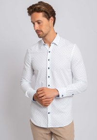 Wit overhemd met lange mouwen, voorzien van een klein blauw geometrisch patroon, een button-down kraag en contrasterende blauwe knopen. Het shirt heeft een getailleerde pasvorm en een soepele textuur.