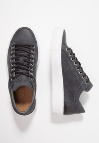 Grå texturerade sneakers med svarta snören, vit gummisula och en slät tåkappa. Har ett subtilt präglat mönster på ovandelen.