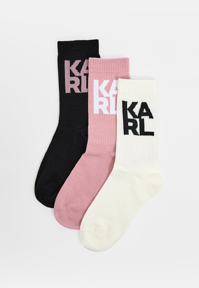 Trzy pary skarpetek załogowych: czarne z różowym logo, różowe z białym logo i białe z czarnym logo. Tekstura prążkowana, mieszanka bawełniana.