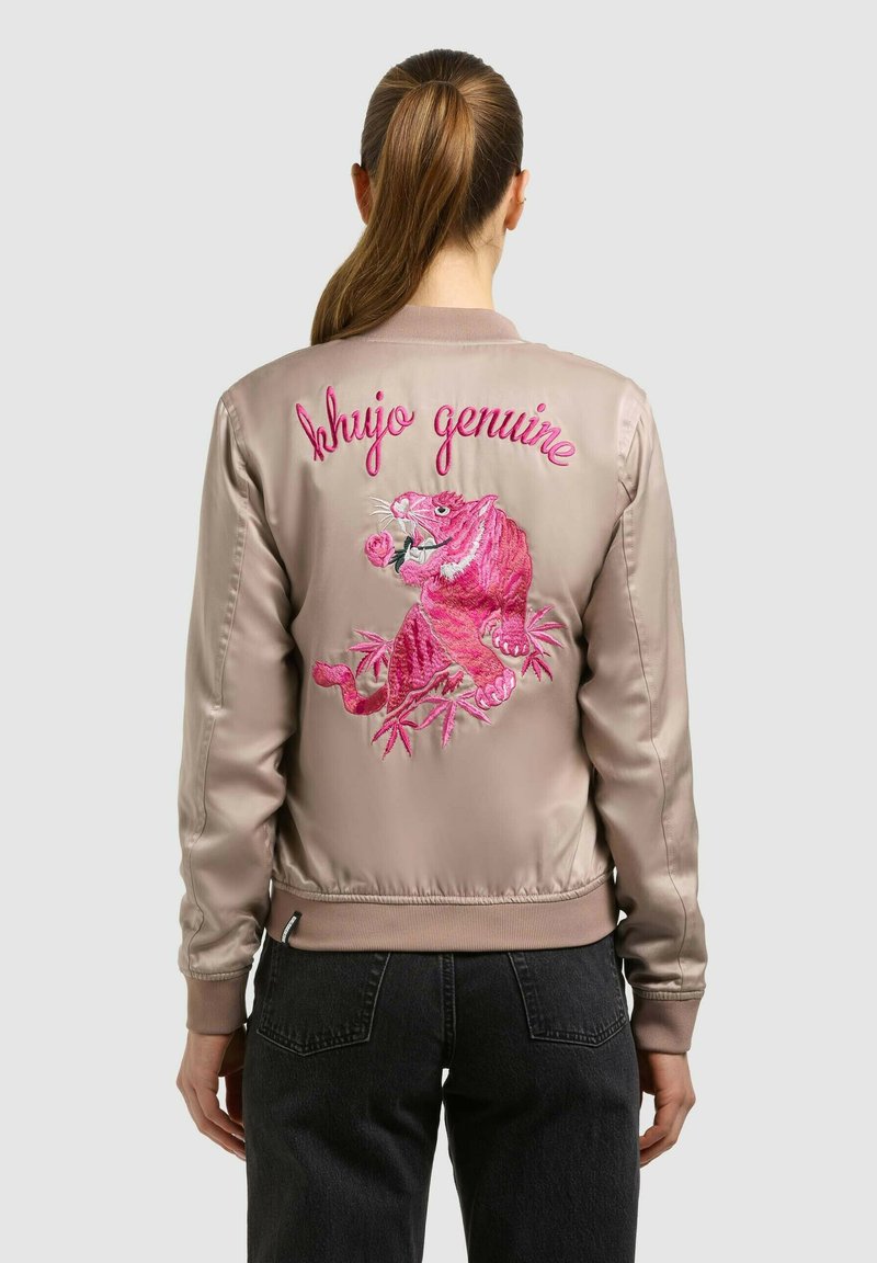 Femme portant un bomber en satin beige avec un tigre rose brodé tenant une rose et le texte « shujo genuine » au dos.