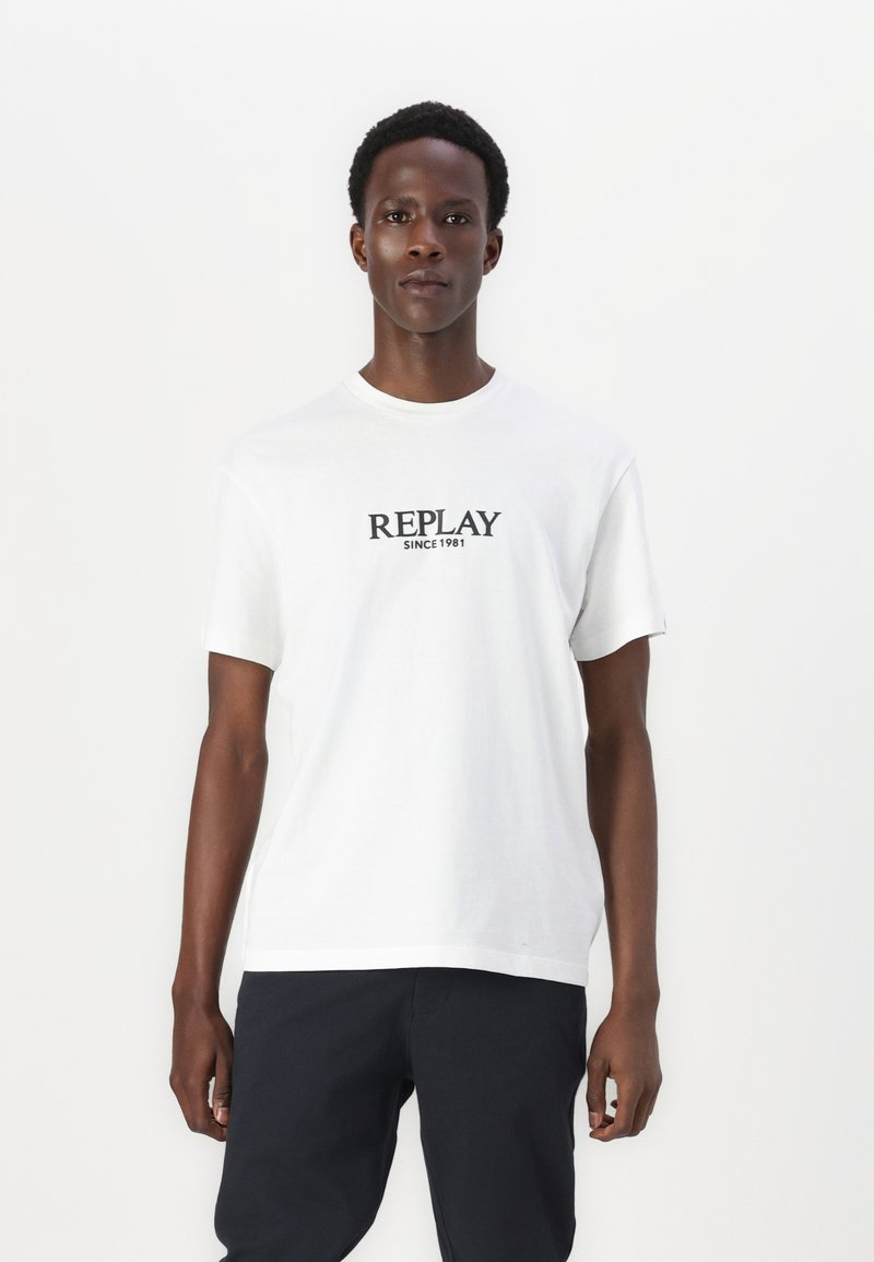 Valge puuvillane T-särk lühikeste varrukatega ja ümarate kaelustega; esiküljel on must "REPLAY" logo tekst ja selle all "SINCE 1981".