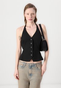 Top nero su misura con scollo a V, cinque bottoni sul davanti e orlo leggermente svasato, abbinato a jeans in denim azzurri.