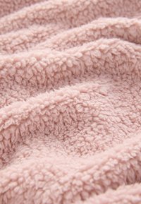 Gestructureerde roze fleece stof met een zachte, pluizige oppervlakte bestaande uit golven en plooien, die de warmte en de luxe kwaliteit benadrukken.