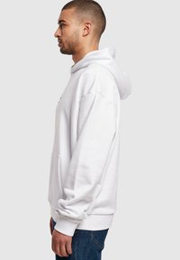 Hvit hettegenser laget av myk stoff, med en frontlomme og avslappet passform, sammen med blå denimjeans.