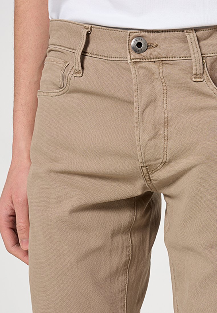 Beżowe spodnie bawełniane o gładkiej teksturze, z zapięciem na guzik z przodu i dwiema bocznymi kieszeniami. Projekt zawiera szlufki na pasek.