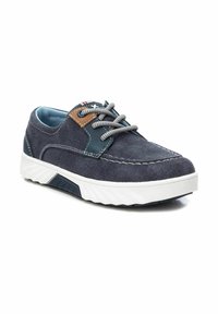 Zapatilla de lona marinera con suela de goma blanca, cordones grises, acento de cuero marrón y detalles cosidos. Presenta una puntera texturizada y un lado con textura.