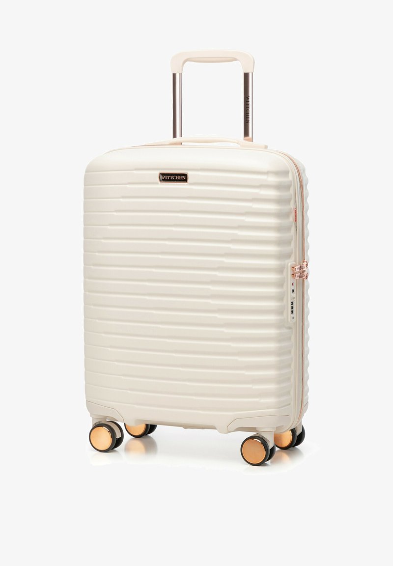 Biała walizka twarda z poziomymi, fakturowanymi rowkami, różowo-złotymi akcentami, podwójnymi kółkami oraz wysuwanym uchwytem dla łatwej manewrowości.