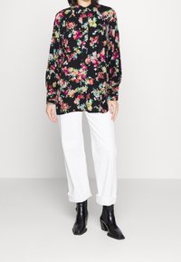 Black floral blouse with multicolored flower patterns, long sleeves, and a buttoned collar, paired with white rolled-up pants and black ankle boots.
