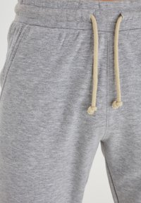 Pantalons de survêtement gris en tissu doux, dotés d'un cordon de serrage avec des accents beiges, de poches latérales et d'un design décontracté.
