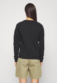 Sudadera negra con mangas raglán y un acabado texturizado, combinada con pantalones cortos caqui, mostrando un ajuste relajado y detalles mínimos.