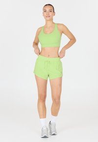 Ljusgrön sportbehå och shorts-set, med elastisk midjeband, lättviktig tyg och en åtsittande design; modell med vita strumpor och grå sneakers.