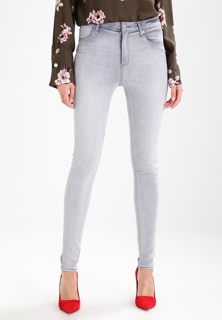 Vaqueros ajustados de color gris claro con una cintura alta y un diseño clásico de cinco bolsillos, hechos de tela de mezclilla. Llevados con zapatos de tacón alto rojos.