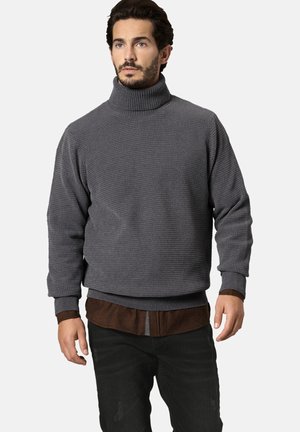 Grauer Strickpullover mit hohem Rollkragen, strukturierter Oberfläche, gerippten Bündchen und Bund, über einem braunen Hemd und schwarzen Hosen getragen.