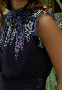 Robe marine ornée d'un imprimé floral dans des nuances de violet, vert et blanc, avec des manches transparentes froncées et un col haut. Tissu lisse et léger.