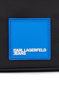 Borsa di stoffa nera con un'etichetta in gomma blu e bianca che riporta la scritta "KARL LAGERFELD JEANS" con cuciture a contrasto.