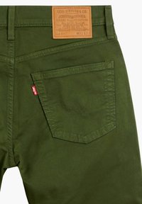 Zelené džíny z bavlněného denimu s hnědou koženou nášivkou, švy na zadní kapse a červenou značkou Levi's na boku. Mají štíhlý střih.