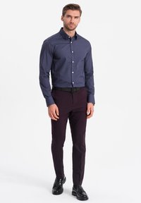 Camisa de botones azul marino con pequeños lunares blancos, combinada con pantalones slim-fit burdeos oscuros y zapatos de cuero negros.