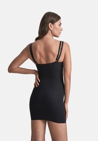 Abito nero aderente con spalline regolabili, cuciture minime e una texture liscia. Presenta una lunghezza corta e un design posteriore discreto.
