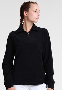 Svart fleece-pulovert med dragkedja i kragen, långärmade och mjukt material. Har en avslappnad passform och en minimalistisk design.