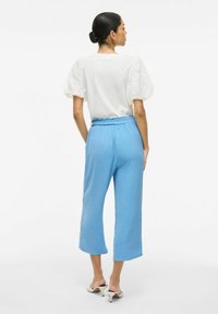 Witte top met geborduurde, puff sleeves, gecombineerd met lichtblauwe, cropped broeken. Gummiband in de taille, gladde textuur en enkel lengte.