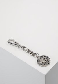 Klíčenka se stříbrným kovovým řetízkem a kulatou visačkou s reliéfním textem. Klip je tvarován pro snadné připevnění.