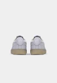 Γκρι δερμάτινα αθλητικά παπούτσια με απλό σχέδιο, με ανοιχτόχρωμη σόλα και διακριτική ανάγλυφη λεπτομέρεια στη φτέρνα.