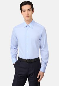 Camicia azzurro chiaro a maniche lunghe con bottoni, realizzata in tessuto misto cotone, caratterizzata da un colletto classico e una leggera lucentezza, abbinata a pantaloni scuri a righe sottili.