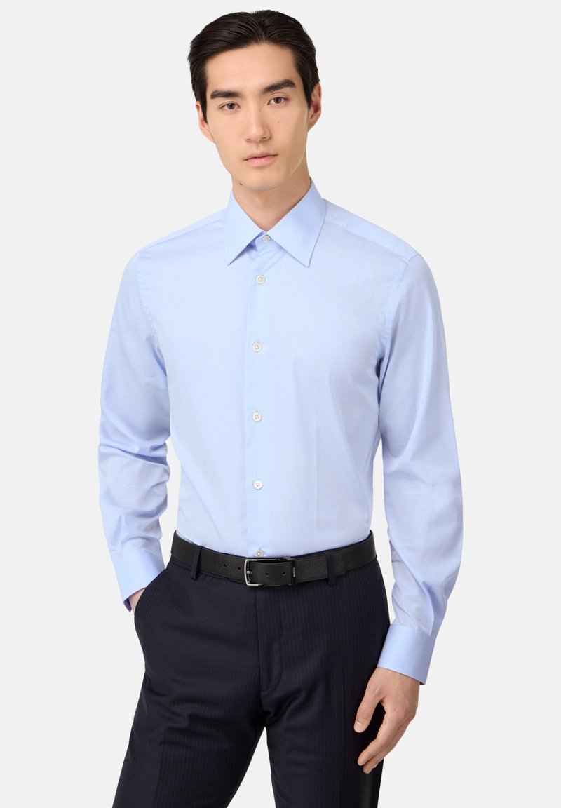 Camicia azzurro chiaro a maniche lunghe con bottoni, realizzata in tessuto misto cotone, caratterizzata da un colletto classico e una leggera lucentezza, abbinata a pantaloni scuri a righe sottili.