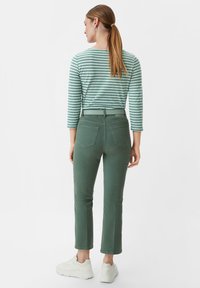 Olivgrüne, schmal geschnittene Hosen mit hoher Taille, Fünf-Taschen-Design und glatter Textur. Kombiniert mit einem gestreiften Langarmoberteil.