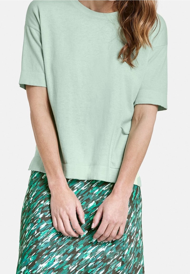T-shirt corto a maniche corte di cotone verde chiaro con scollo rotondo, abbinato a una gonna verde e marrone con un motivo a fantasie astratte e pennellate.