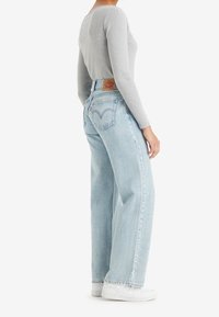 Ljusblå högmidjade jeans med rak passform, mjuk denimtextur och tydlig sömnad på bakfickorna. Kombineras med en grå ribbad topp.