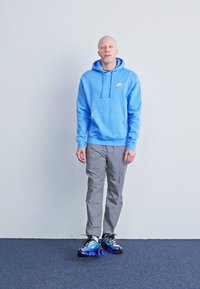 Hoodie Nike azul claro, calças cinza e sapatilhas desportivas em gradiente preto-azul. O hoodie apresenta um bolso frontal e capuz com cordão.