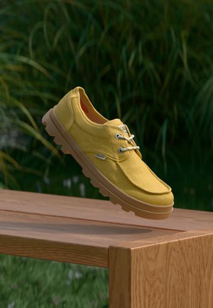 Chaussure en toile jaune avec un bout arrondi, une semelle en caoutchouc et des lacets. Les détails remarquables comprennent des accents cousus et un logo latéral.