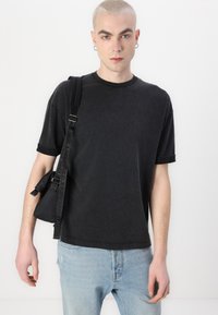 Svart bomullströja med rundad halsringning och uppvikt ärm, parat med ljusblå denimjeans och en svart väska med en märkesremsa.