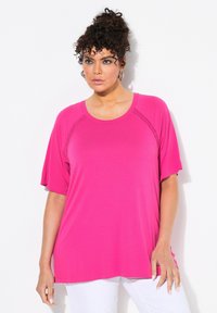 Top corto fucsia a maniche corte con scollo rotondo e fessure laterali. Il tessuto appare liscio con una vestibilità comoda e cuciture dettagliate lungo le spalle.