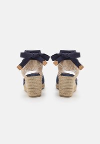Námornícke espadrilky na vysokom podpätku so zos woven jute podpätkom, otvoreným dizajnom a námorníckymi stuhami priviazanými okolo členku.