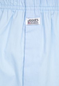 Ljusblå bomullsshorts med elastiskt midjeband, med en vit etikett som står "JOCKEY USA Originals." Slät textur, enkl design.