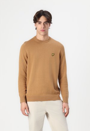 Pull couleur camel en matériau doux, avec un col rond, des manches longues et un petit logo brodé jaune sur la poitrine.