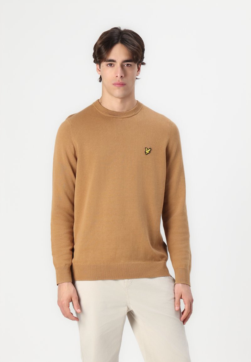 Pulover camel barve, narejen iz mehkega materiala, z okroglim izrezom, dolgimi rokavi in majhnim rumenim vezenim logotipom na prsih.