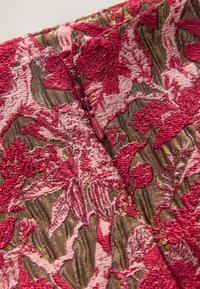 Vezeni materijal s cvjetnim uzorkom u ružičastim i zlatnim tonovima, sa vidljivim patentnim zatvaračem na teksturiranoj podlozi.