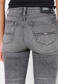 Jeans de denim gris delgados con una textura desvaída, que cuentan con dos bolsillos traseros y un pequeño logo de la marca en la cinturilla.