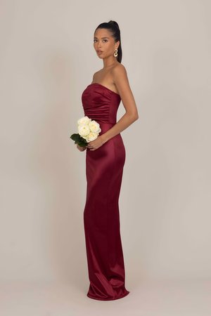 Robes sans bretelles bordeaux avec corsage froncé et silhouette ajustée, fabriquées en satin lisse. Le modèle tient des roses blanches et des feuillages.