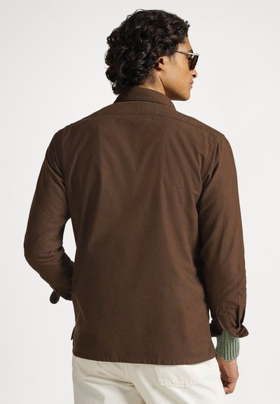 Καφέ πουκάμισο με κουμπιά, μακριά μανίκια, με υφή και πράσινες πλεκτές λεπτομέρειες στα μανίκια. Το σύνολο συμπληρώνεται με λευκό παντελόνι.