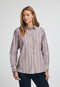 Camicia con bottoni in morbido tessuto di cotone, caratterizzata da righe verticali rosa e bianche, colletto arrotondato e polsini con bottoni. Logo discreto sul petto.