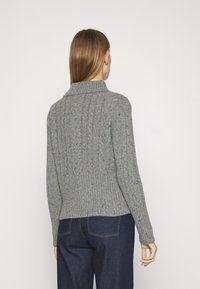 Grå stickad tröja med ribbad nederkant och texturerade mönster. Har en vikbar krage och flerfärgade prickar över hela tyget.