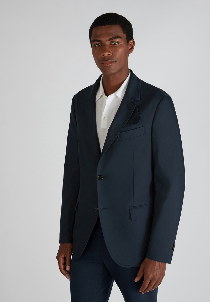 Marineblazer aus glattem Stoff, einreihig mit zwei Knöpfen, mit Revers und einer Brusttasche. Trägt man über einem weißen Hemd mit Kragen.