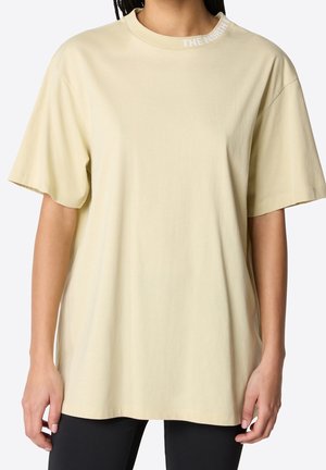 Jasnożółta, oversize bawełniana koszulka z krótkimi rękawami i prążkowanym, okrągłym dekoltem, z białym logo nadrukowanym na kołnierzu.